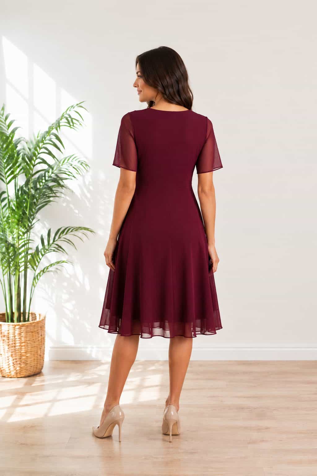 Ženska nosi eleganntno bordo midi obleko s prosojnimi kratkimi rokavi in lahkotnim padajočim krilom, primerno za poroke, praznovanja in druge posebne priložnosti.