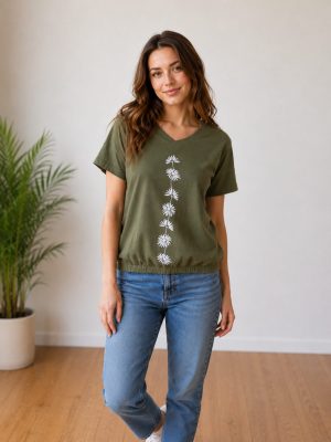 Ženska nosi majico s tiskom. Majica ima kratke rokave, V-izrez in je olivne barve.