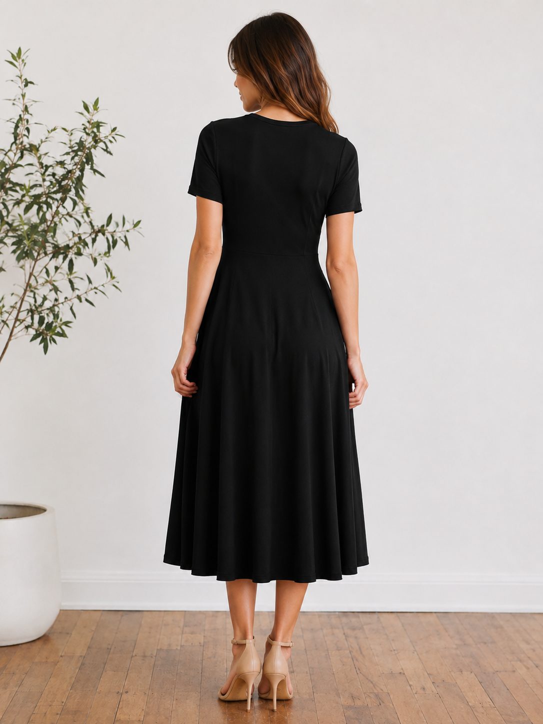 Ženska nosi elegantno midi obleko. Obleka ima ženstven kroj, ki lepo poudari silhueto,